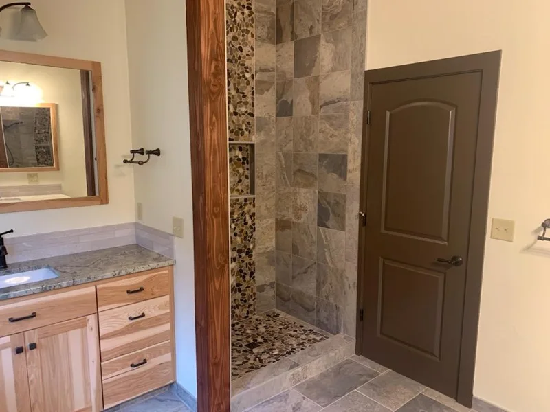 Remodeled bathroom with pebble-accent tile shower by OJEG Construction