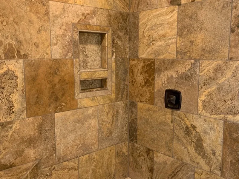 Custom travertine walk-in shower with bench and storage niche